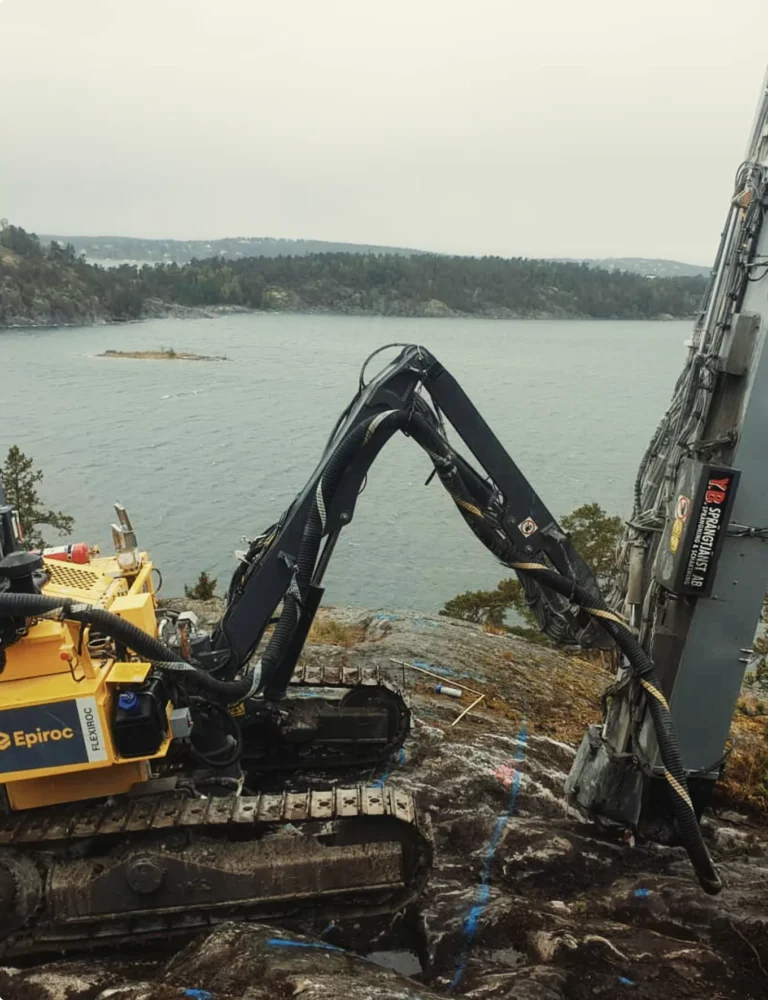Bergspräckning Stockholm med borrigg på svårtillgänglig bergshäll vid vattennära miljö.