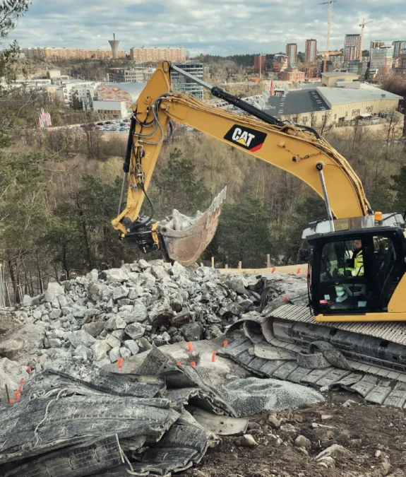 Bergspräckning Stockholm med grävmaskin som avlägsnar krossat berg på byggarbetsplats.