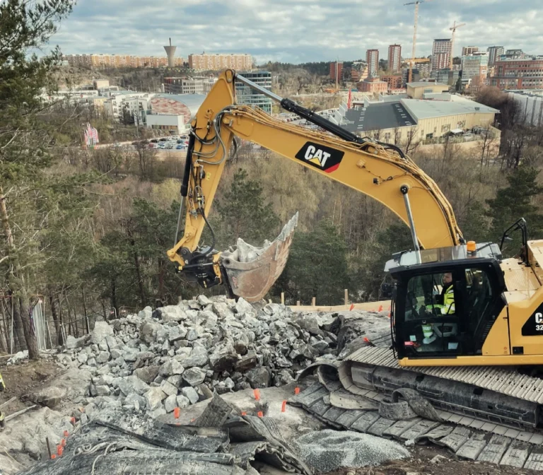 Bergspräckning Stockholm med grävmaskin som avlägsnar krossat berg på byggarbetsplats.
